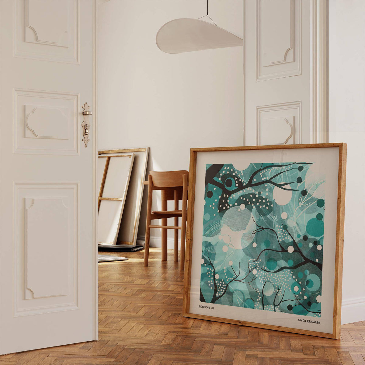 Print leaning on a wooden floor showing abstract moonlit branches in teal and black near a chair