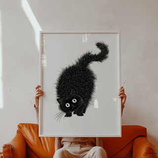 Framed close-up of the Arched Back Cat Print showing a black arched back cat illustration held by a person on a brown sofa