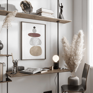 Abstract rock art print with stacked minimalist shapes in neutral colours on a desk with lamp and books