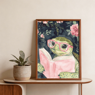 Framed Turtle Reading Art Print with pink glasses and book next to a plant on a table