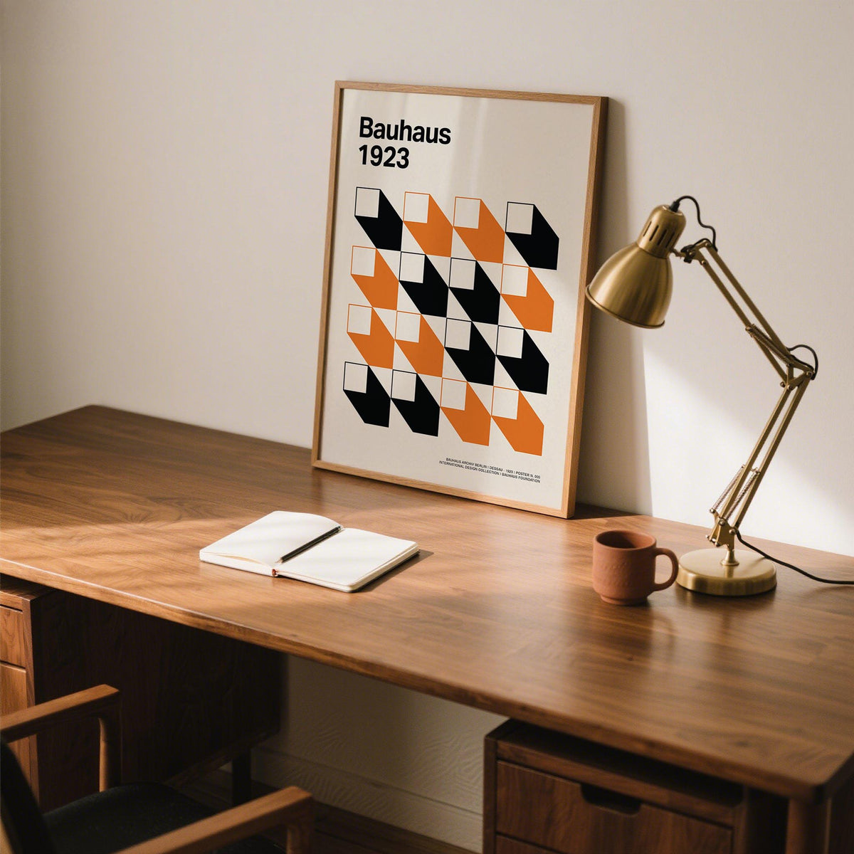 Artwork for Office leaning on desk with orange and black geometric grid beside gold desk lamp