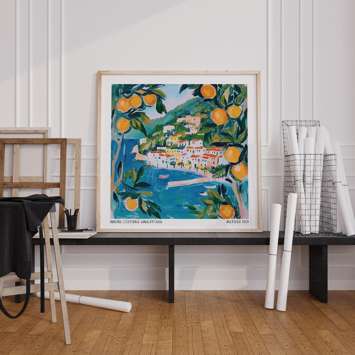 Amalfi wall art of a coastal village with oranges in blue and green tones leaning on a shelf by rolled prints