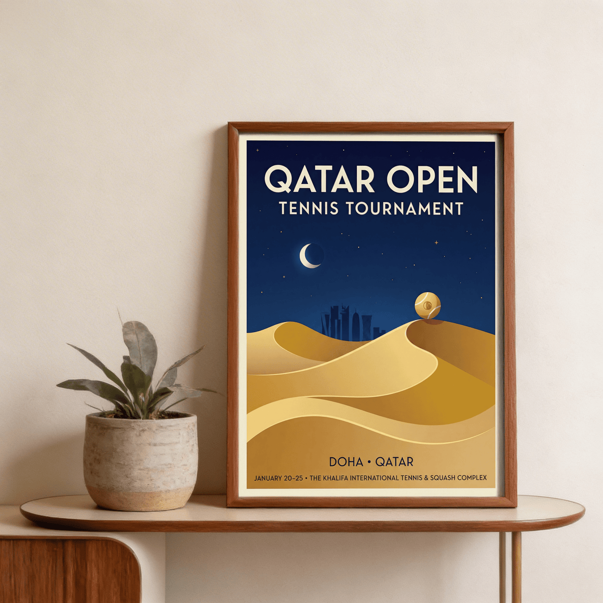 Framed Qatar Open Tennis Print with a tennis ball on sand dunes next to a plant on a table