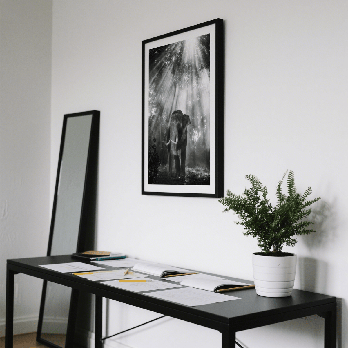 Nature Photography wall art of an elephant in a forest with light rays hanging above a desk with a plant