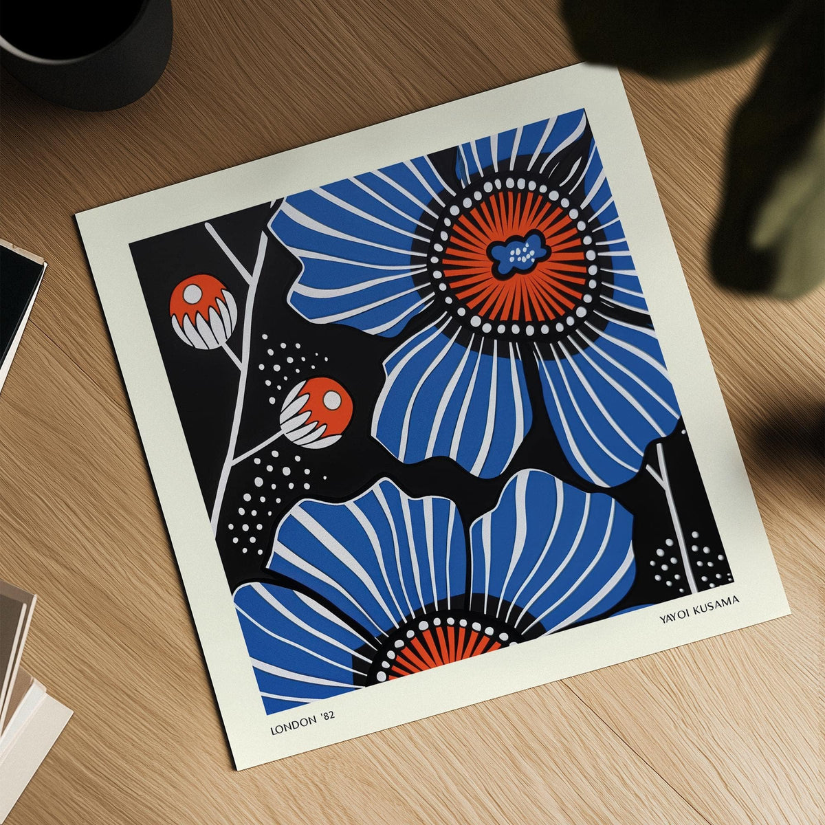 Blue poppy flower illustration with white dots detail on a wooden surface next to cup and leaves