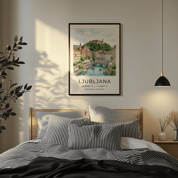 Framed Ljubljana art print of a river view with boats in soft watercolour above a bed with striped pillows
