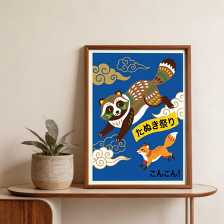 Framed Japanese Animal Art Print with a dancing raccoon and fox on a blue background on a wooden sideboard next to a plant
