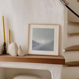 Gray and white wall art of person on winding path leaning on a shelf with decorative objects sideways
