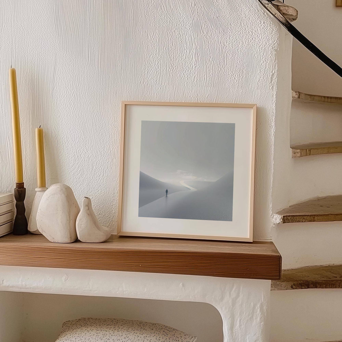 Gray and white wall art of person on winding path leaning on a shelf with decorative objects sideways