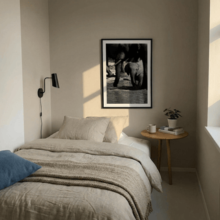 Nature art print of baby and adult elephants in black and white above a bedside table with a plant