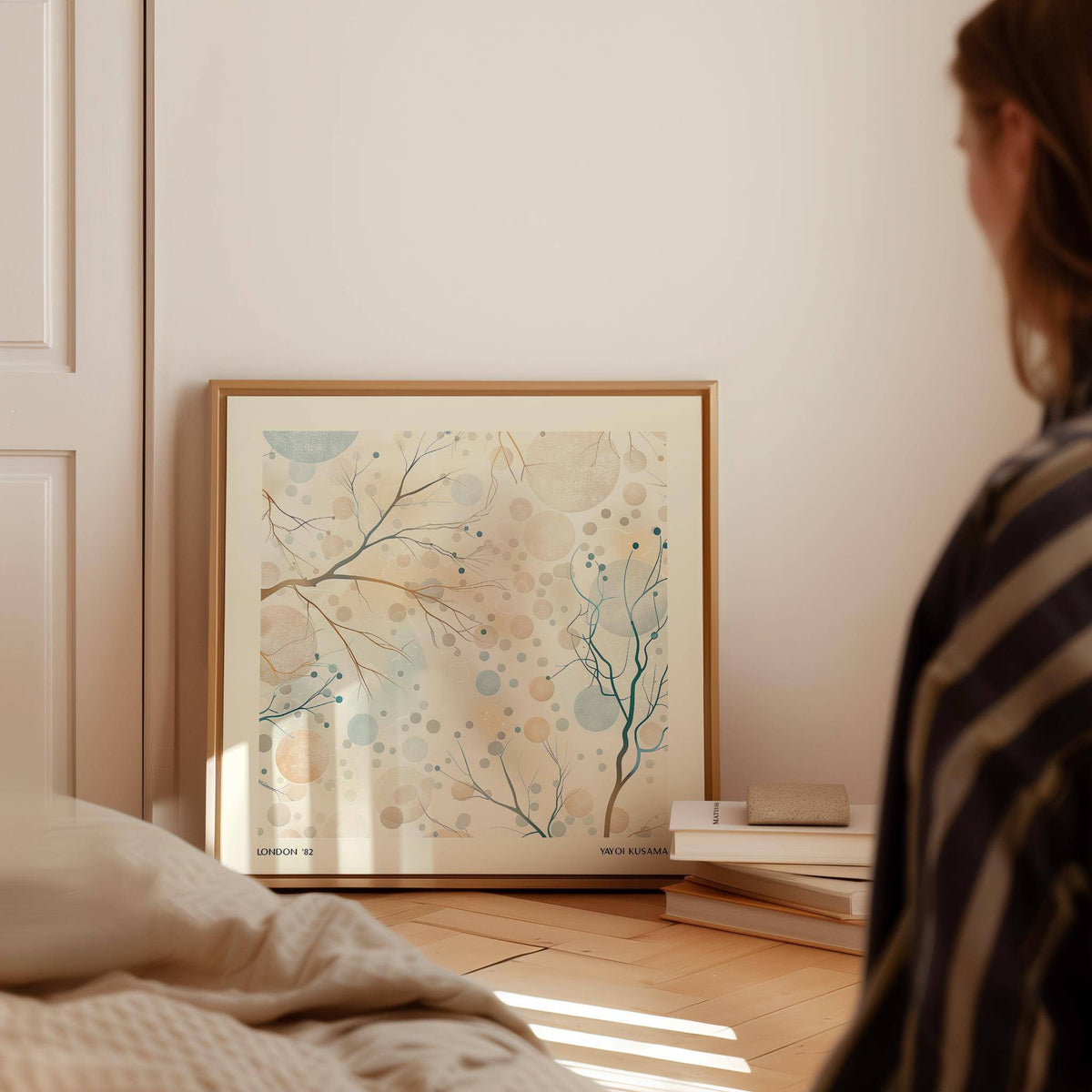 Neutral artwork leaning on floor with delicate branches and blue and beige circles beside books