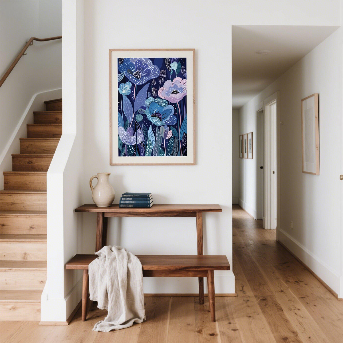 Purple home decor print of abstract blue and lavender flowers above a wooden bench with a jug and books in a hallway