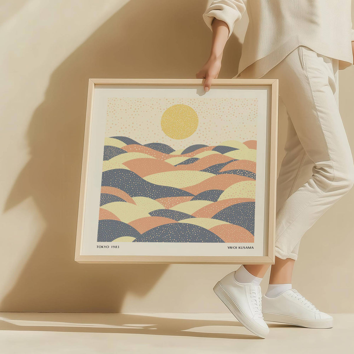 Framed Pastel Wall Art held by a person featuring abstract hills with a sun in soft yellow, pink and blue
