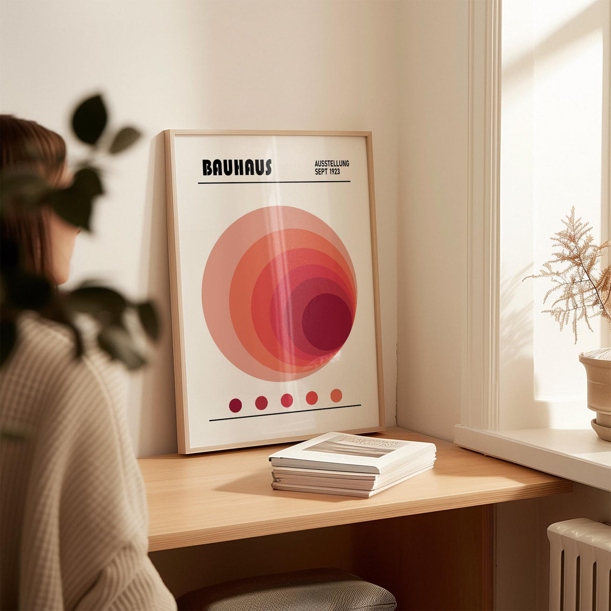 Wall Art Office leaning on a desk featuring concentric circles in pink and red with a stack of books nearby