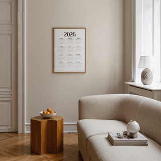 Minimalist wall calendar framed on a beige wall above a wooden side table with a bowl in a living room