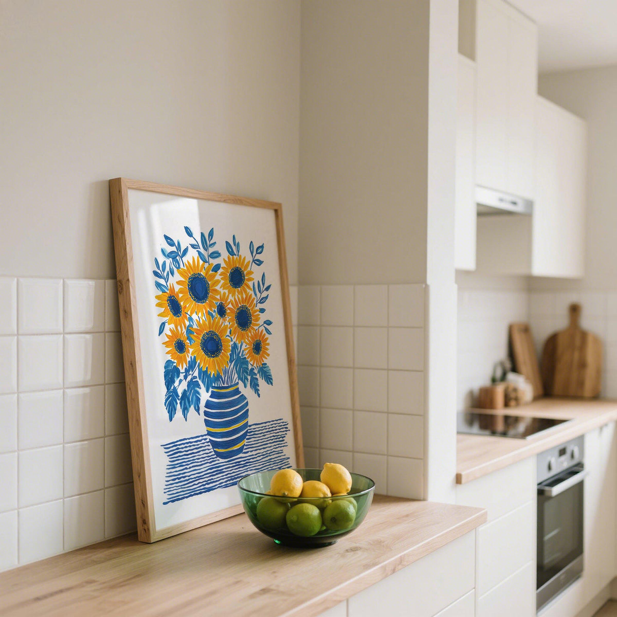 Print leaning on a kitchen counter with sunflowers in blue and yellow vase and green fruit bowl