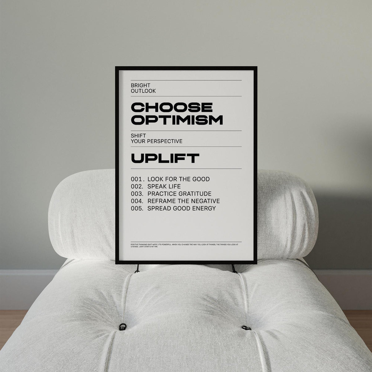 Framed choose optimism motivational wall art print with black text on white background on a white cushioned chair