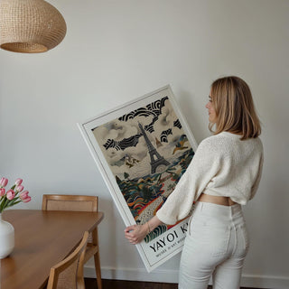 Framed Eiffel Tower print held by a woman with abstract clouds and landscape in muted colours