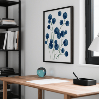 Watercolor flower wall art of blue botanical flowers in a black frame above a wooden desk with a glass paperweight