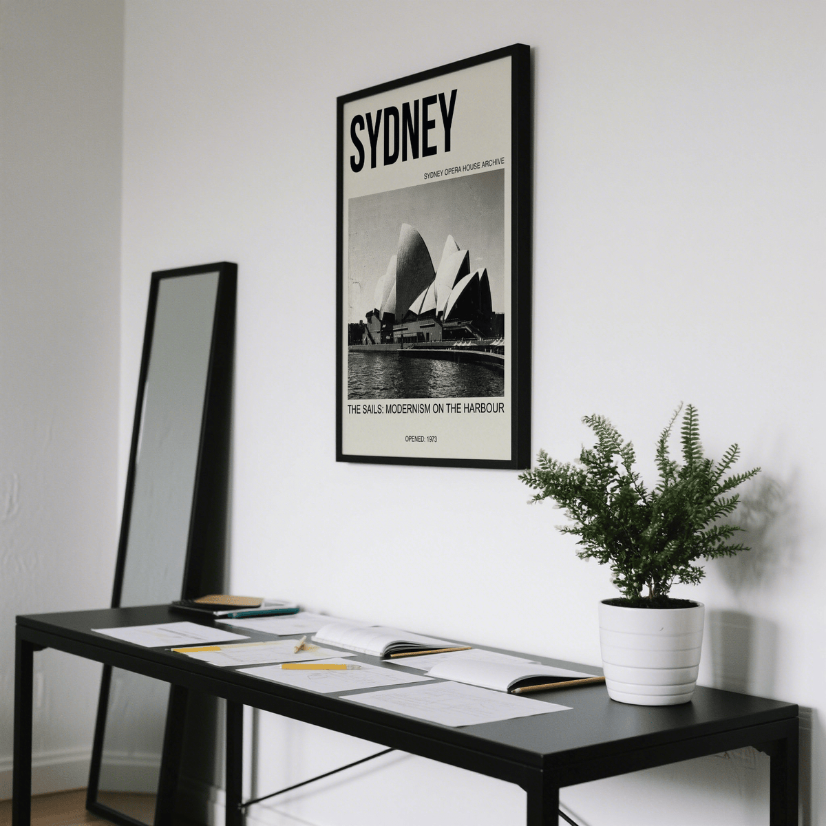 Sydney Opera House Poster on a white wall above a black desk with papers and a potted plant