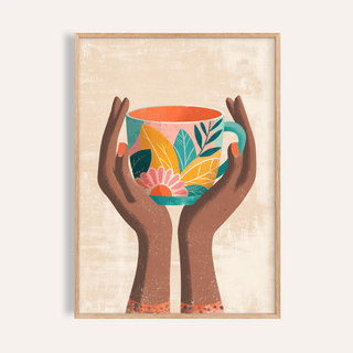 Framed print of hands holding a colourful floral mug in teal, yellow and pink on beige