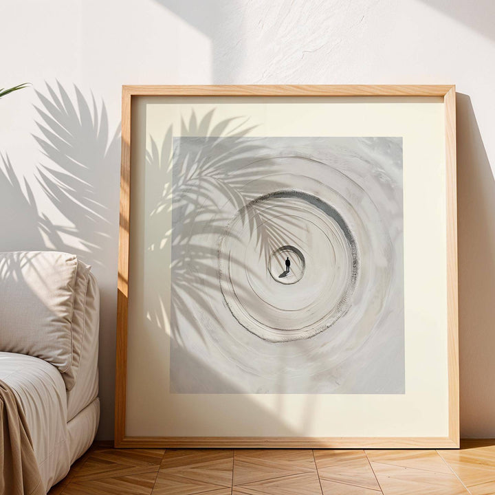 Framed print of concentric sand circles in beige and grey hues with palm leaf shadow above sofa