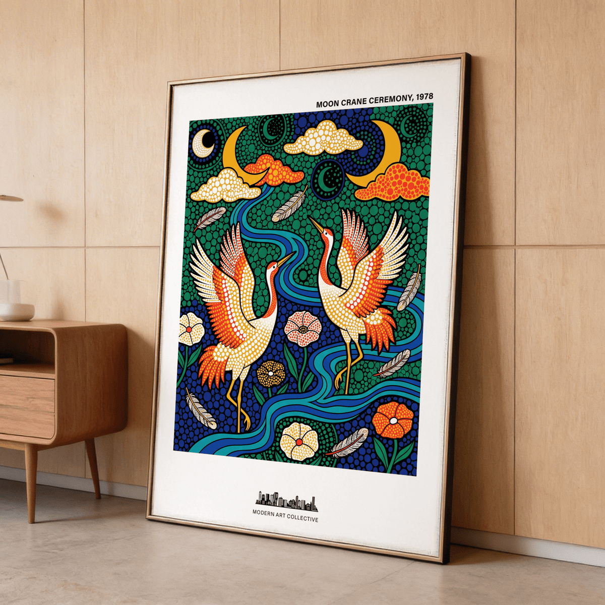 Print leaning on floor of colourful crane poster with dancing cranes in folk art style near wooden cabinet