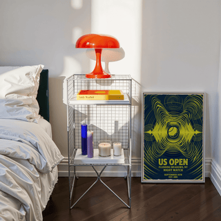 Tennis Night Art Print leaning on a wooden floor beside a bedside table with a red lamp and candles