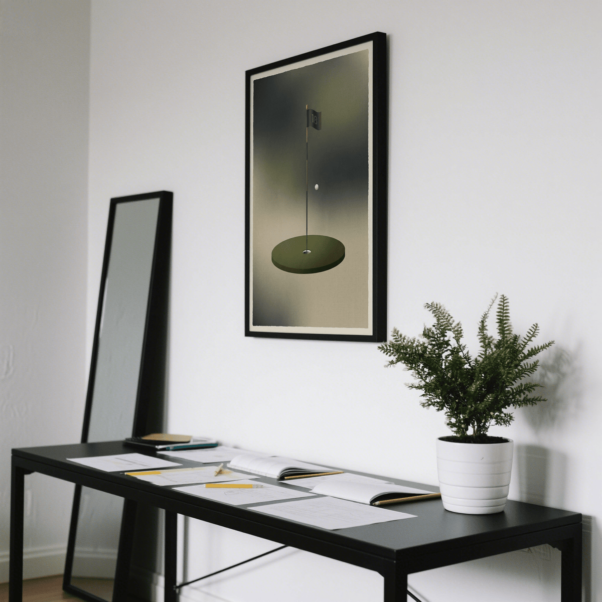 Minimalist golf wall art of a golf hole and ball in muted green and grey hung above a black desk with a potted plant