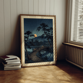 Moonlit Bridge Art Print leaning on a floor next to a stack of books in a room with wall paneling and window blinds