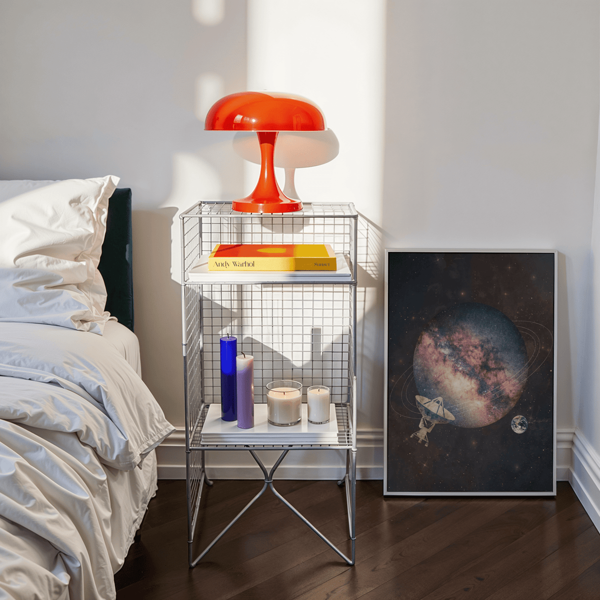 Print leaning with cosmic art print of abstract planet and satellite beside a wire bedside table with red lamp