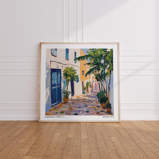 Morocco wall art of a Mediterranean street scene with blue doors and green plants leaning on wooden floor
