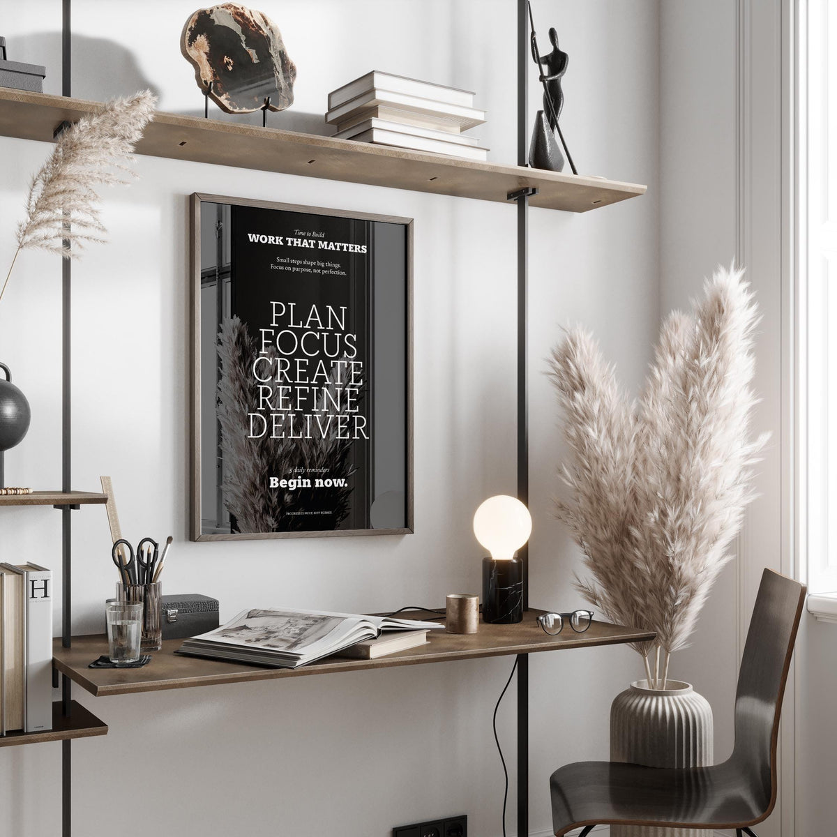 Inspiring wall decor framed print with white text on black hung above a wooden desk with a vase of pampas grass