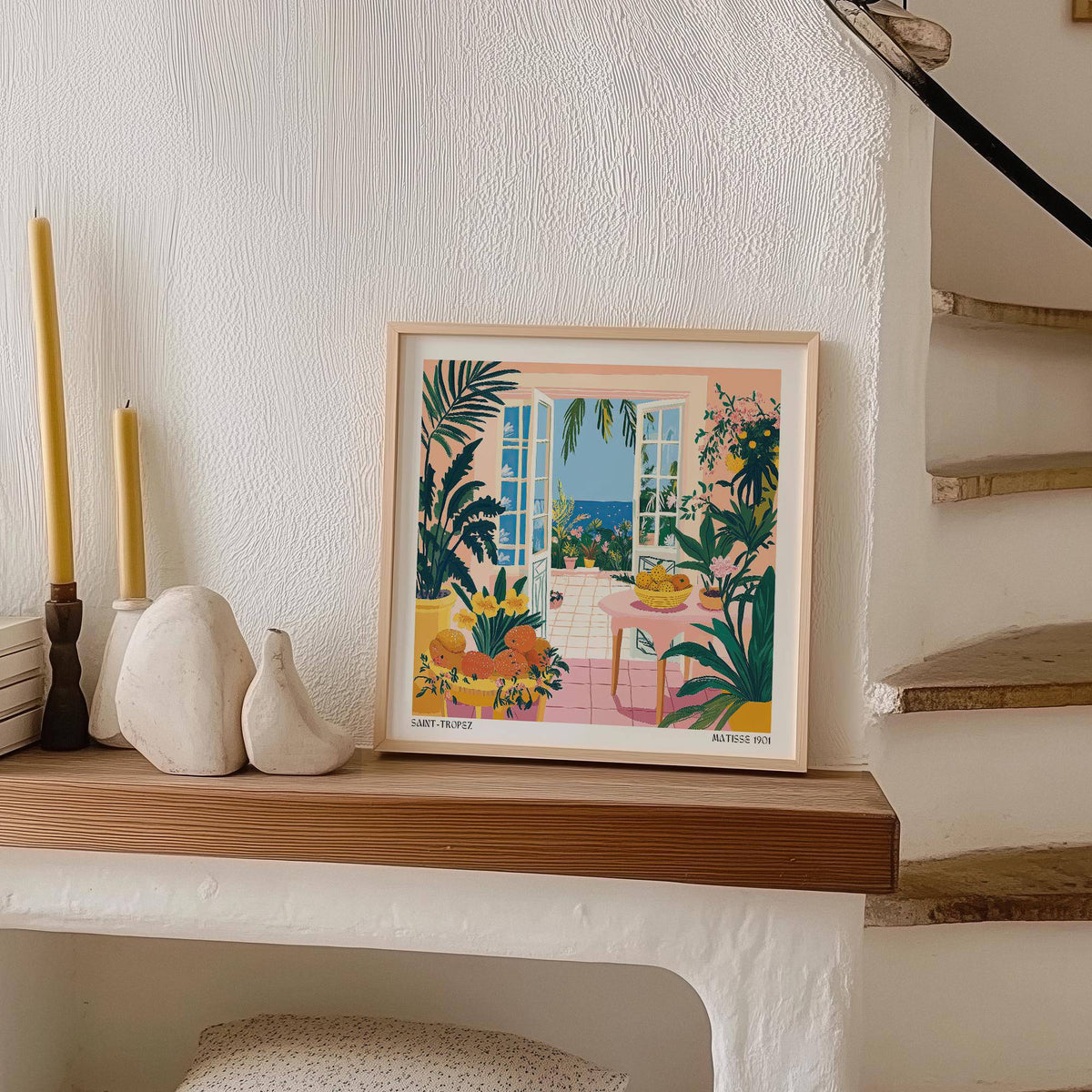 Coastal wall art framed print with open doors and sea view leaning on a wooden shelf next to candles
