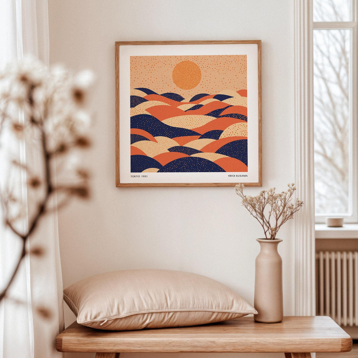 Abstract wall art colourful showing abstract hills and sun in blue and orange hanging above a wooden table with a beige cushion and vase