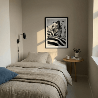 Zebra black white wall art above bed with beige bedding and blue cushion in a bedroom with a side table