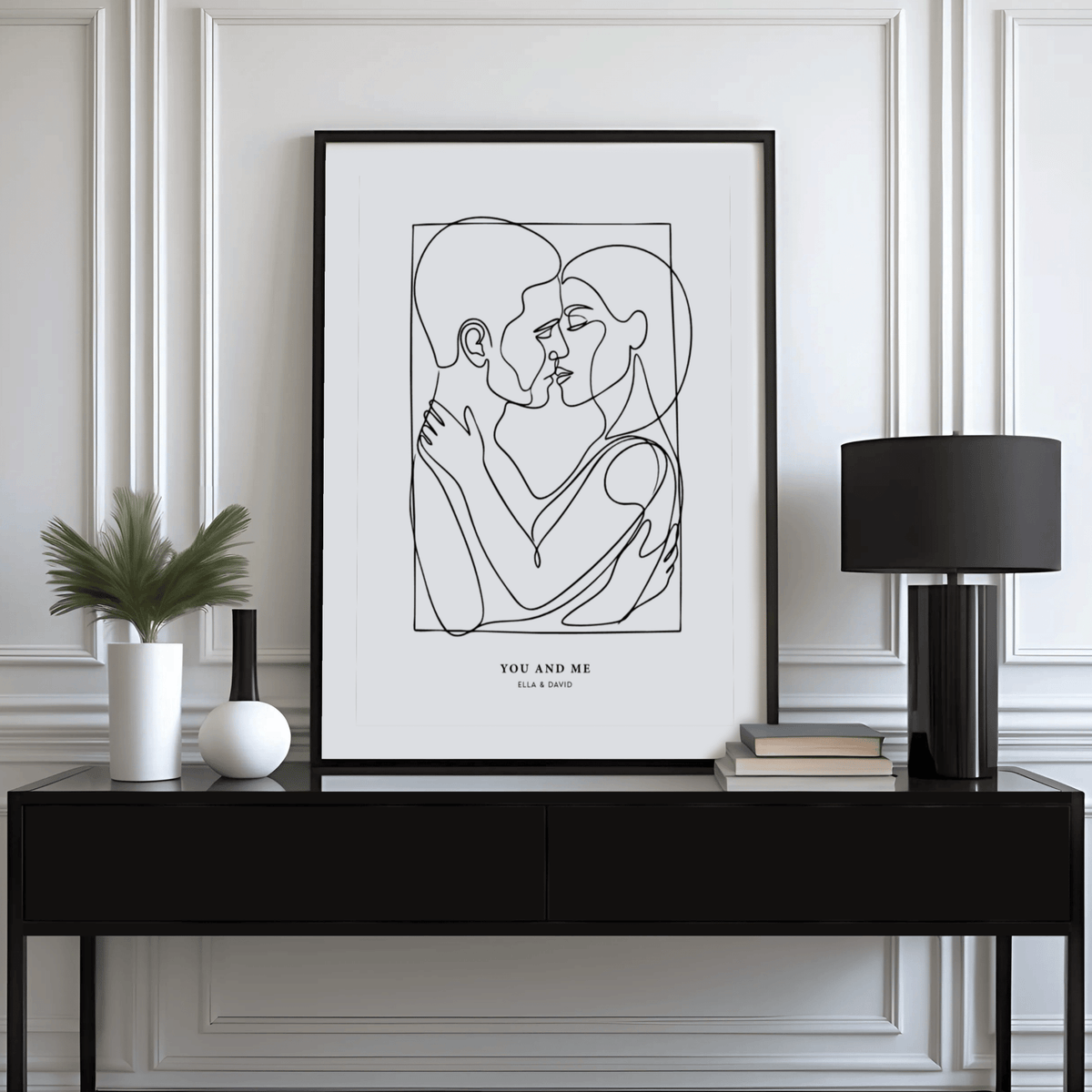 Abstract Figures print of an embracing couple in black line art on a white background on a console table with lamp and plant