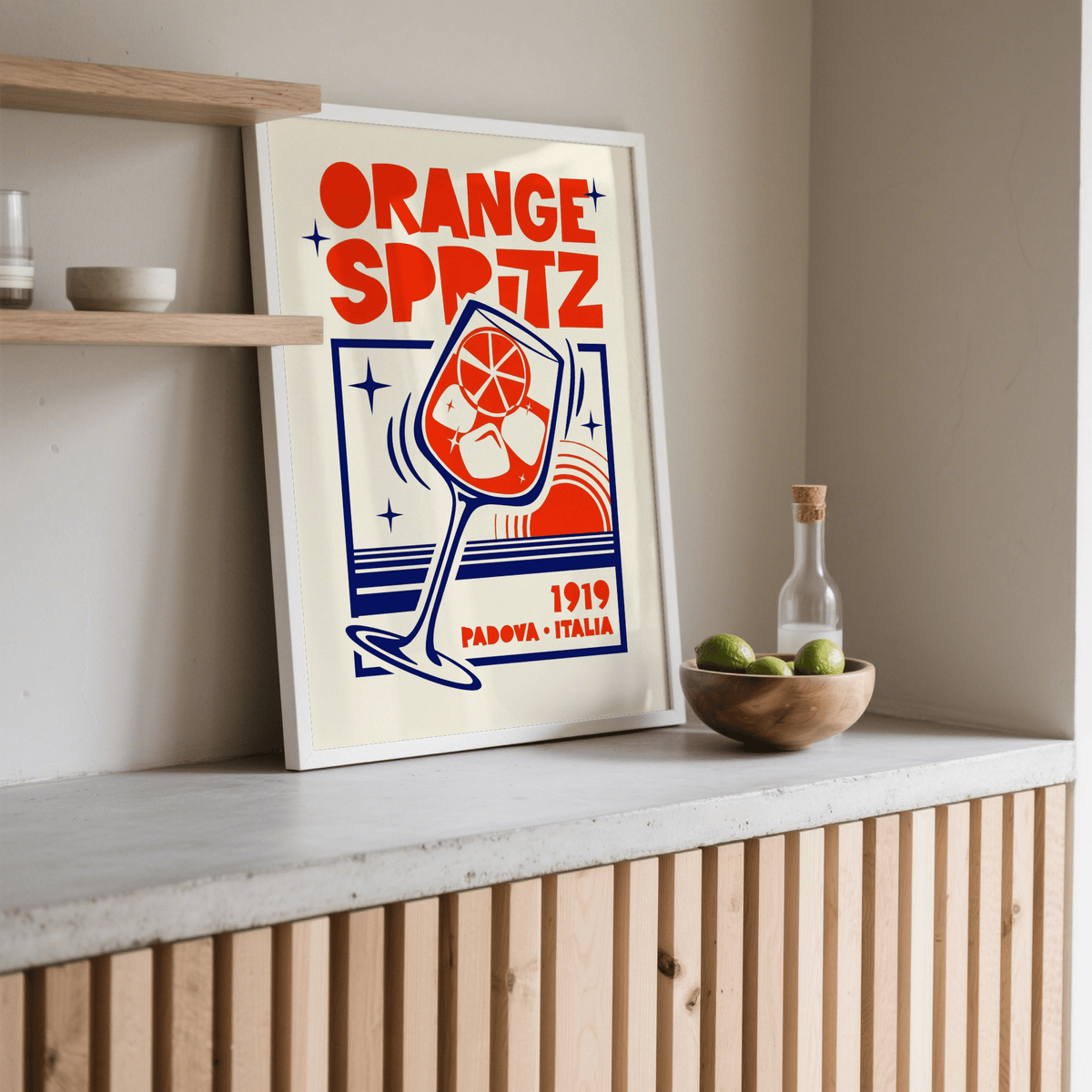 Print leaning on a shelf of an orange spritz cocktail in retro style with a wooden bowl of limes nearby