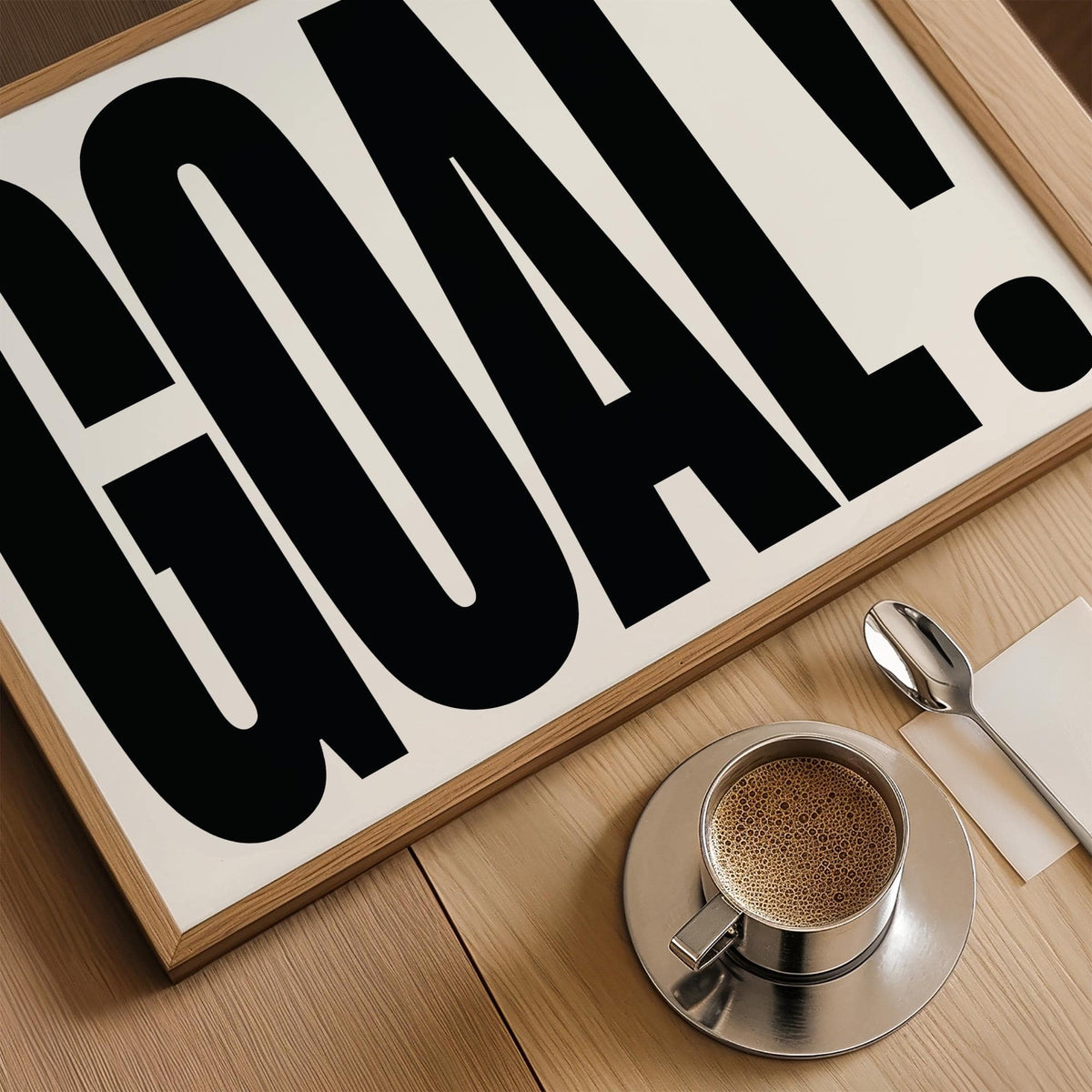 Close-up of wall art for games room with bold GOAL typography in black on white and cup of coffee