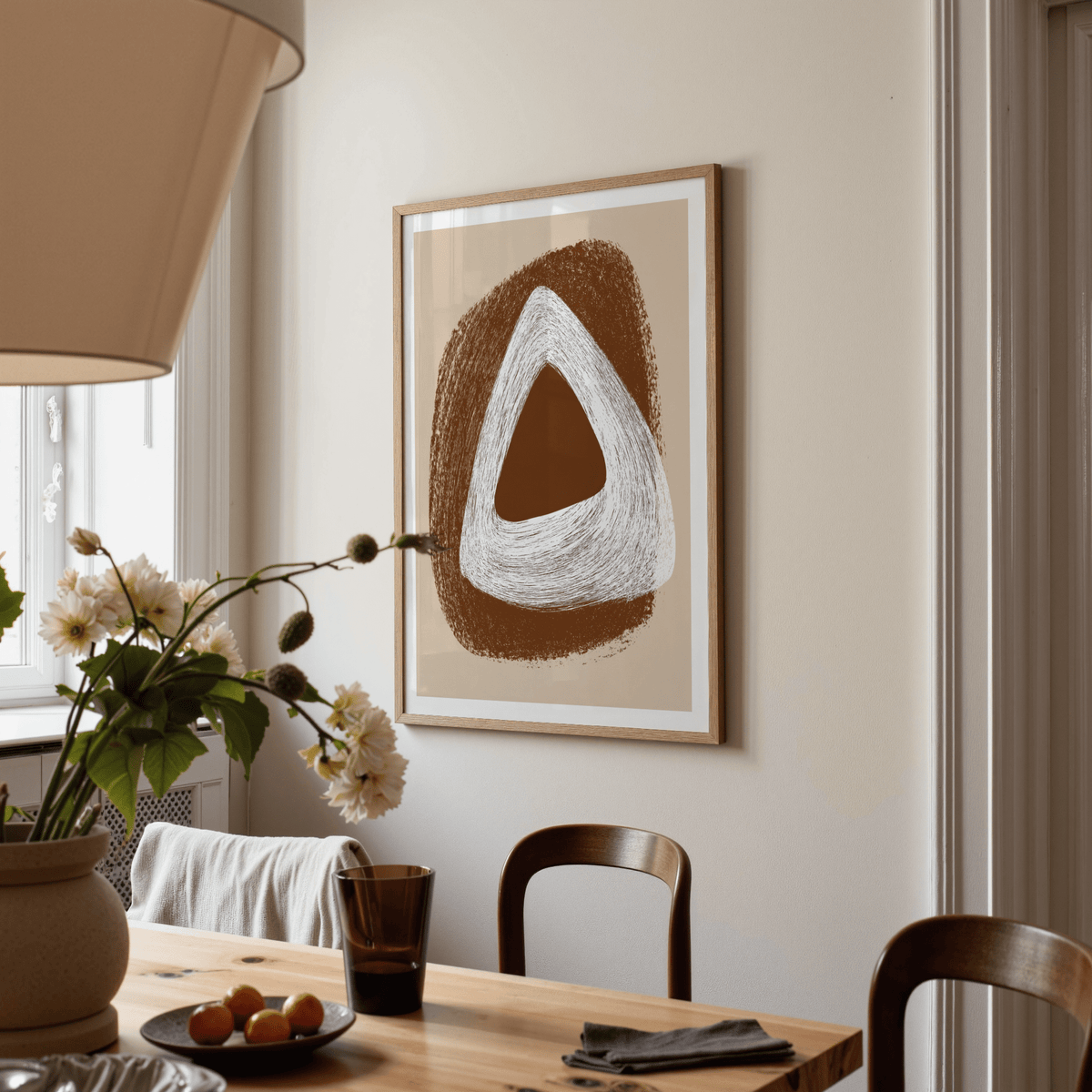 Framed Boho Geometric Art Print with abstract triangle shapes in brown and white in a dining room with a flower vase