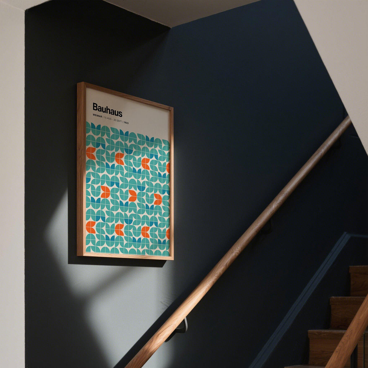 Graphic wall art with a geometric pattern in teal and orange on a dark grey stairwell wall with wooden handrail