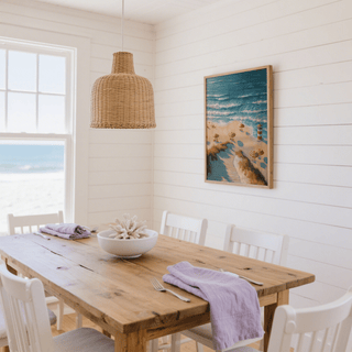 Print on a wall of a striped beach lighthouse and umbrellas in soft blues and oranges in a dining room with wooden table