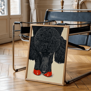 Print leaning on a floor next to a black leather chair showing poodle wall art with red shoes and a beige background