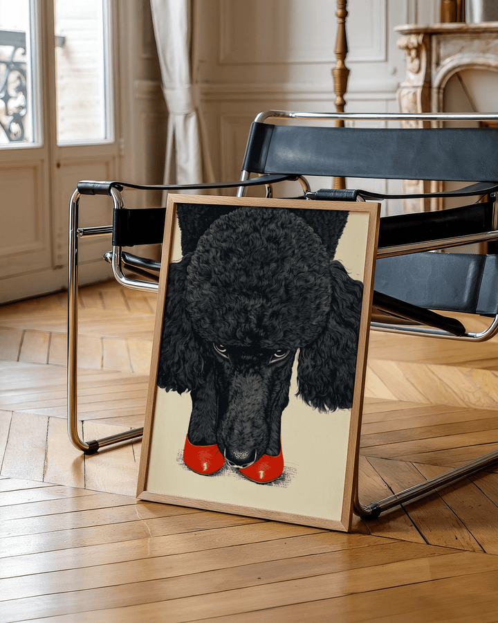 Print leaning on a floor next to a black leather chair showing poodle wall art with red shoes and a beige background