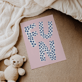 Fun Typography wall art with white letters and blue spots on a pink background lying beside a teddy bear on carpet