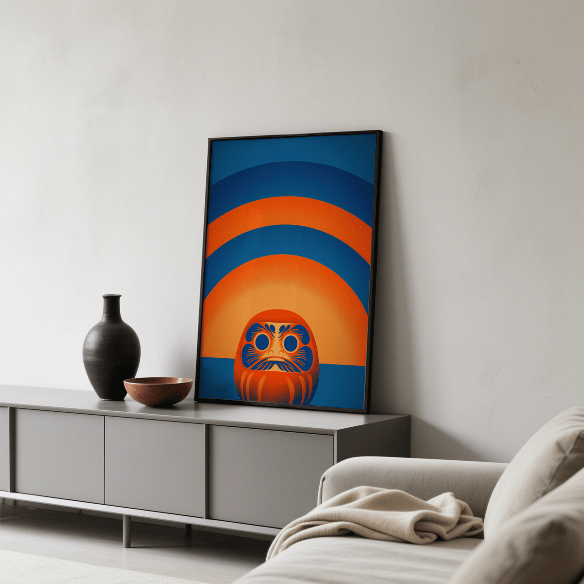 Print leaning on a grey cabinet with ceramic vase and bowl showing an orange and blue daruma doll illustration
