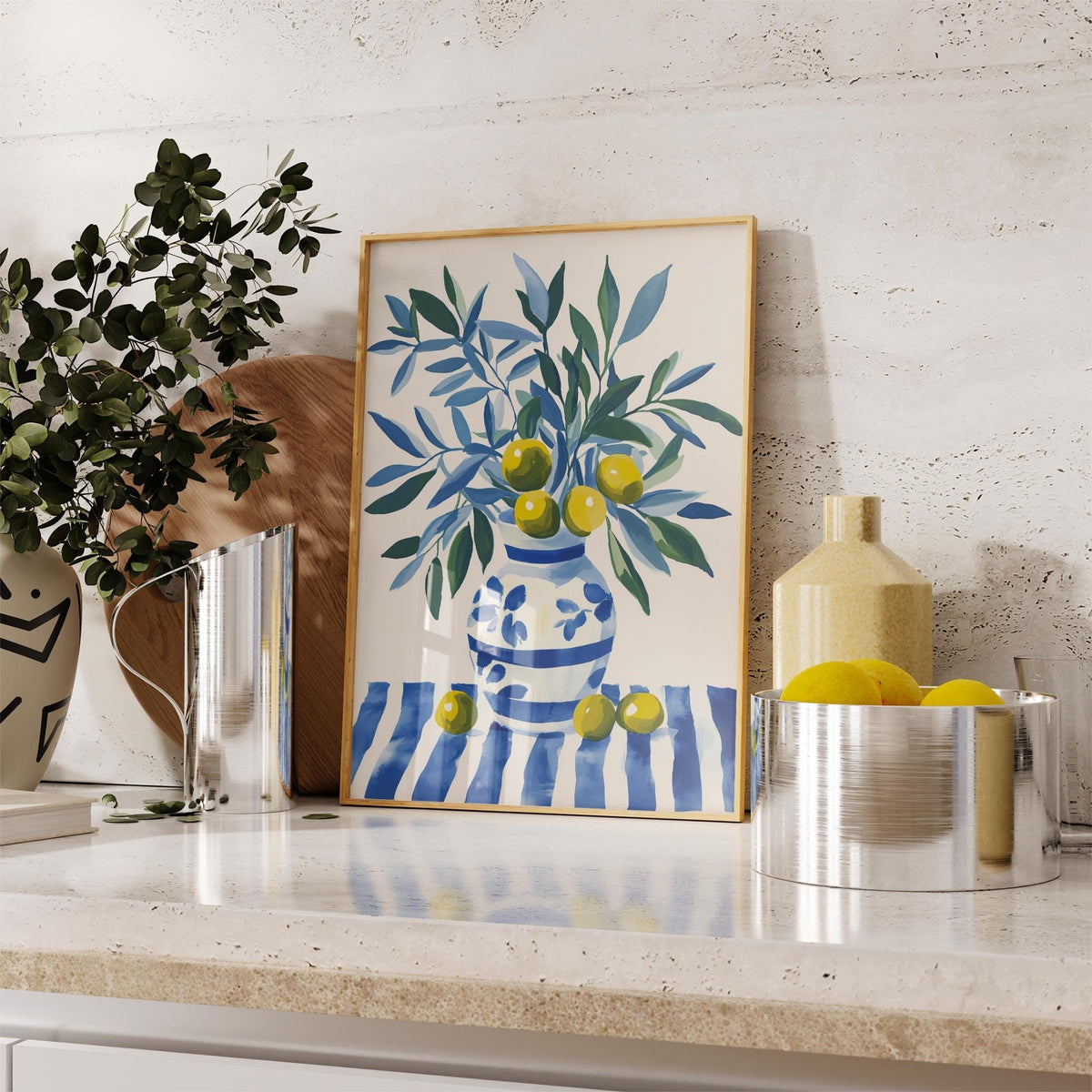 Framed Olive Tree wall art showing a blue and green olive branch in a blue and white vase on a stone shelf next to a metal fruit bowl