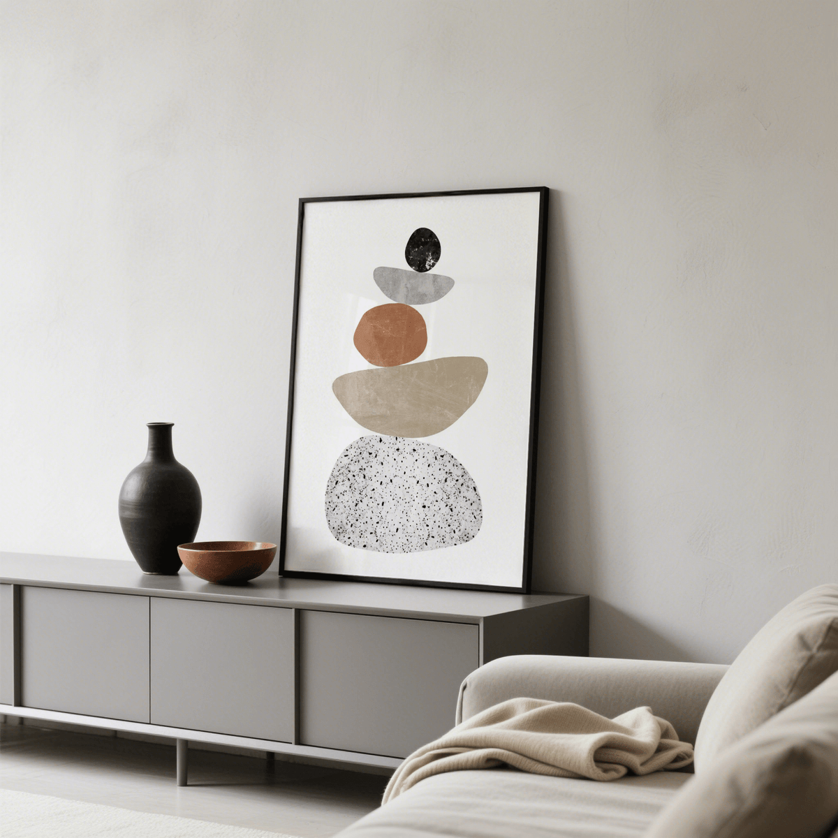 Modern Pebble Print leaning on a grey sideboard next to a black vase and wooden bowl in a living room
