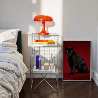 Black Panther Art Print leaning on the floor beside a white bed and metal bedside table with an orange lamp in bedroom