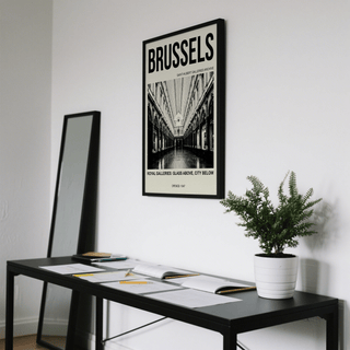 Brussels Gallery Print hanging above a black table with papers and a green plant on it in a room
